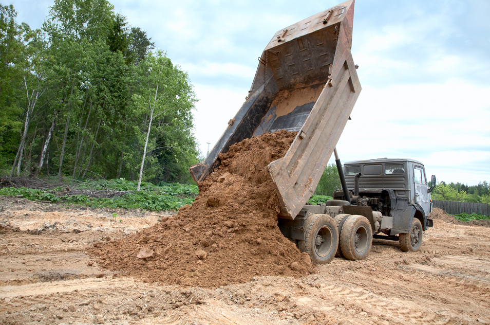 Overholt Grading - dump truck dumping dirt in clearing surrounded by trees